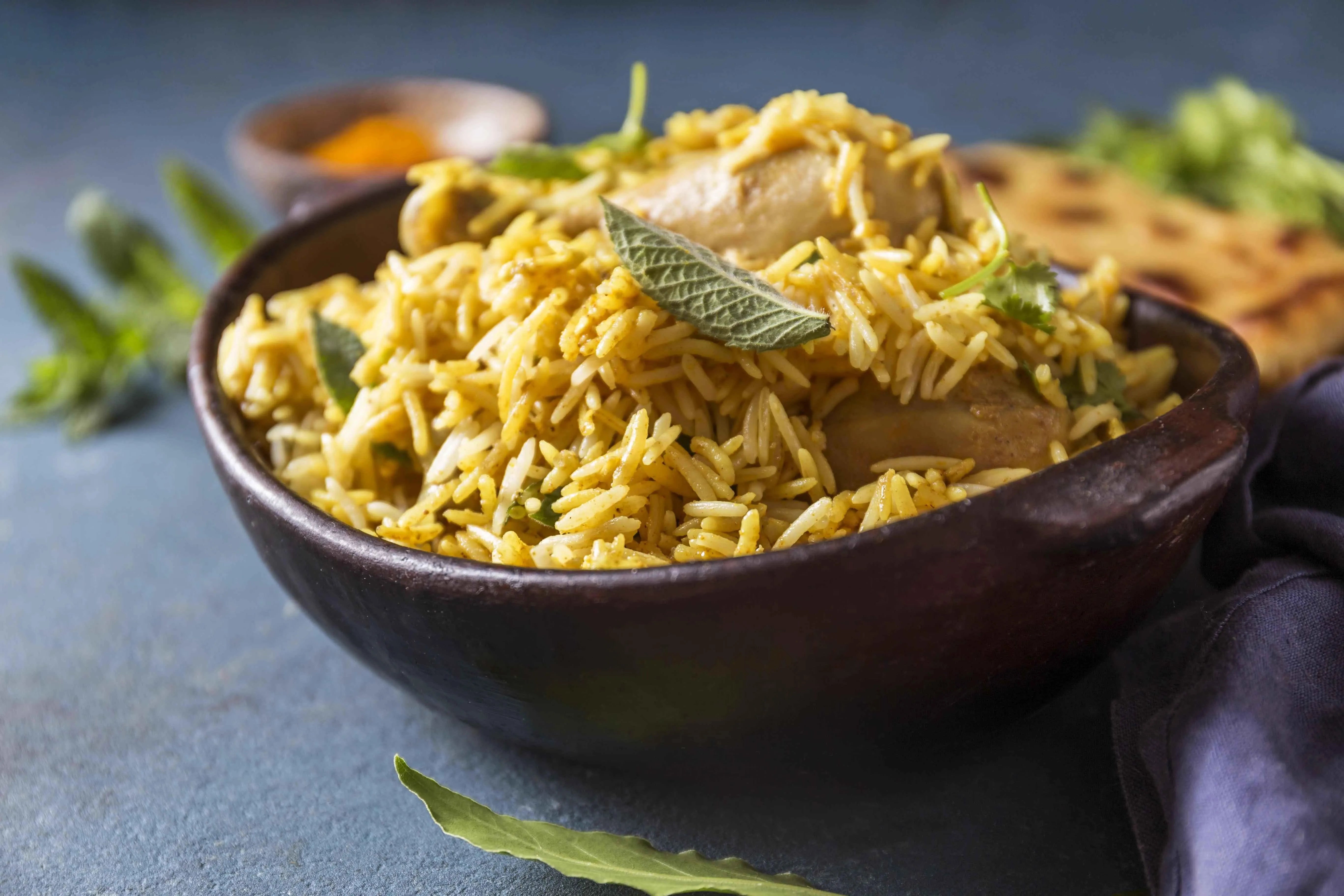 Chicken biryani with basmati rice, herbs, and naan bread in a rustic bowl