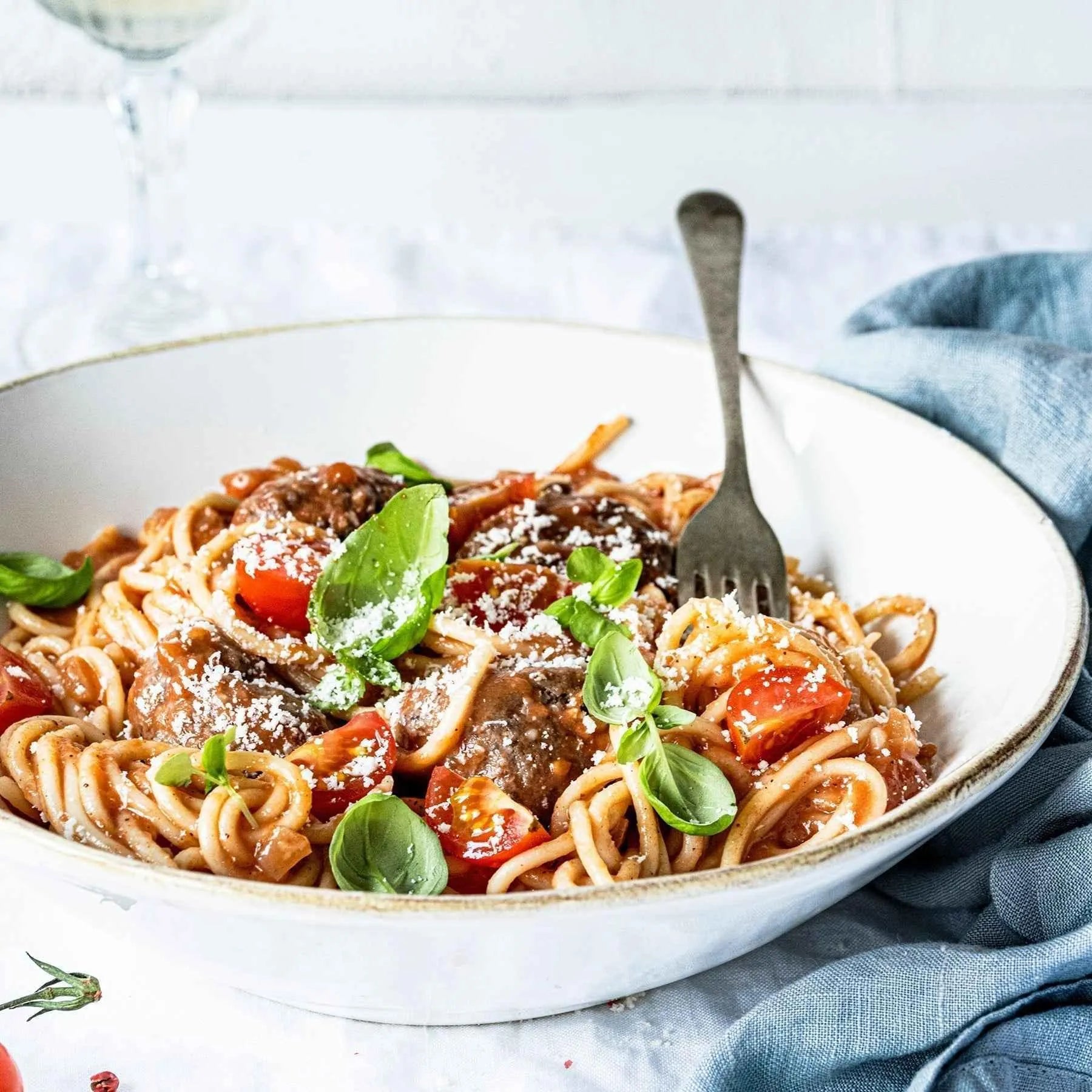 Spaghetti with meatballs, tomato sauce, fresh basil and grated cheese in a white bowl