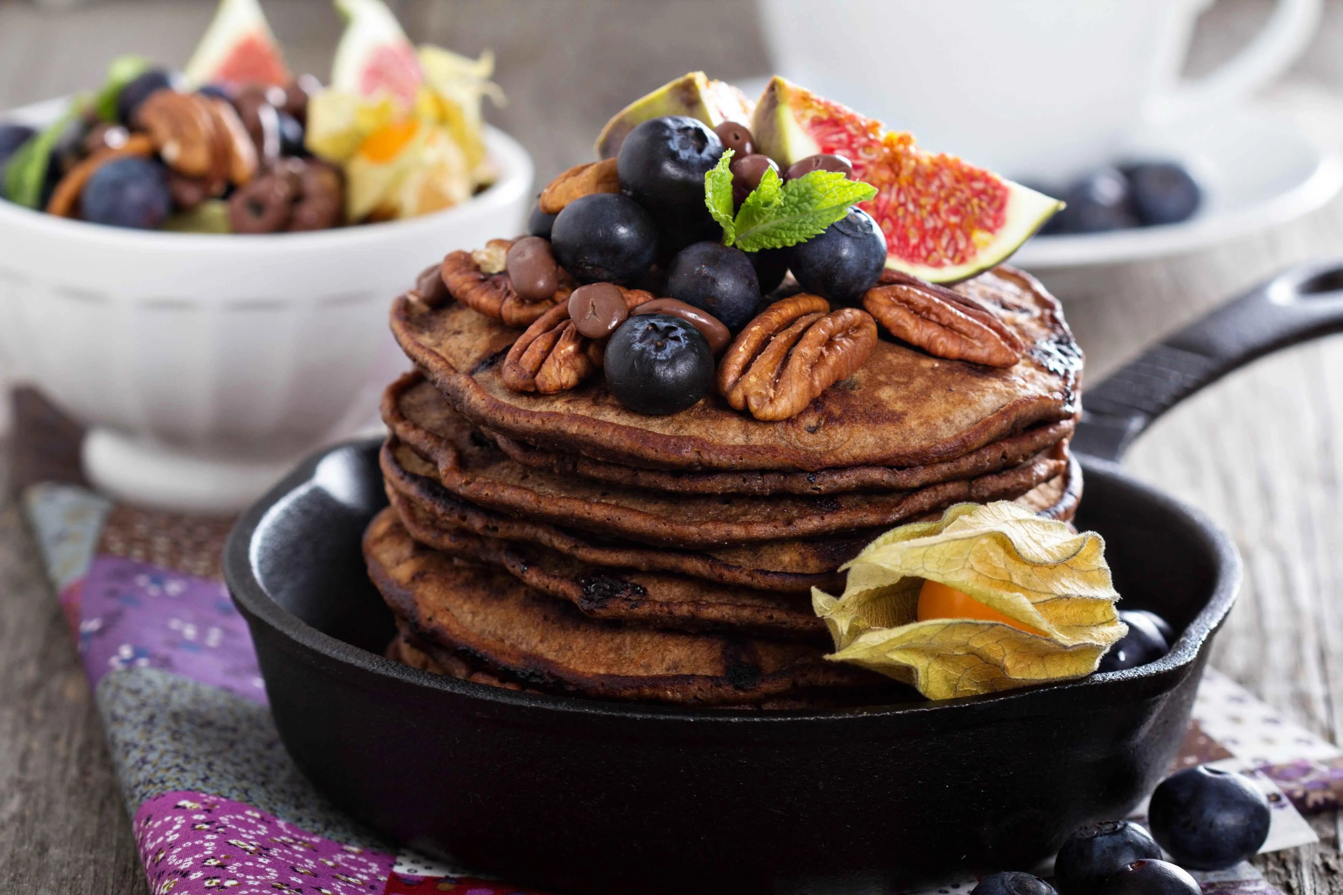 Stack of chocolate pancakes with blueberries, pecans, figs, and mint in a skillet
